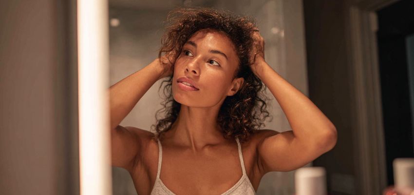 Woman checking her curly hair in the mirror, applying hair care tips for salon clients