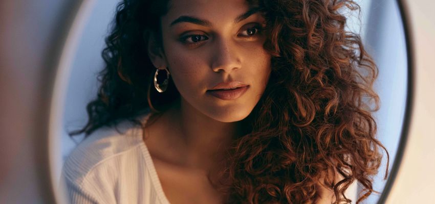 Close-up of a woman with gorgeous voluminous curls, answering can you wash your hair before a perm with healthy hair results.