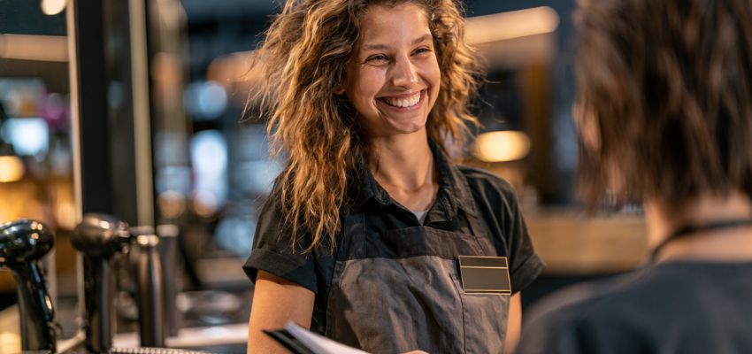 Friendly young hairstylist smiling at a client, illustrating how much do hair stylists make in the industry