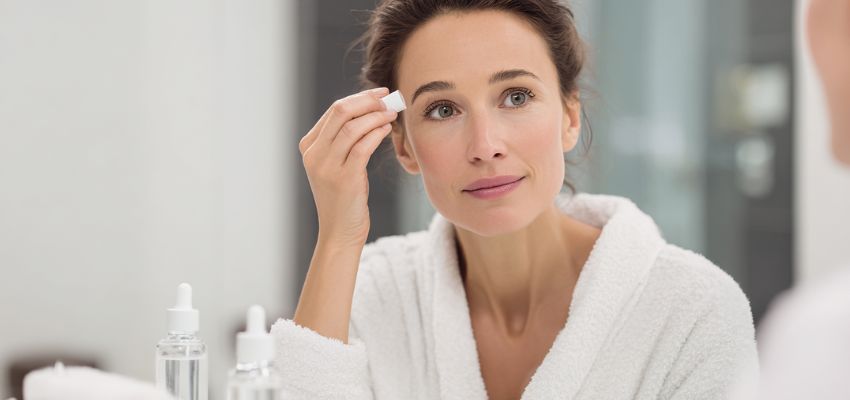 Woman in a white robe prepping her eyebrows for an eyebrow tinting session.