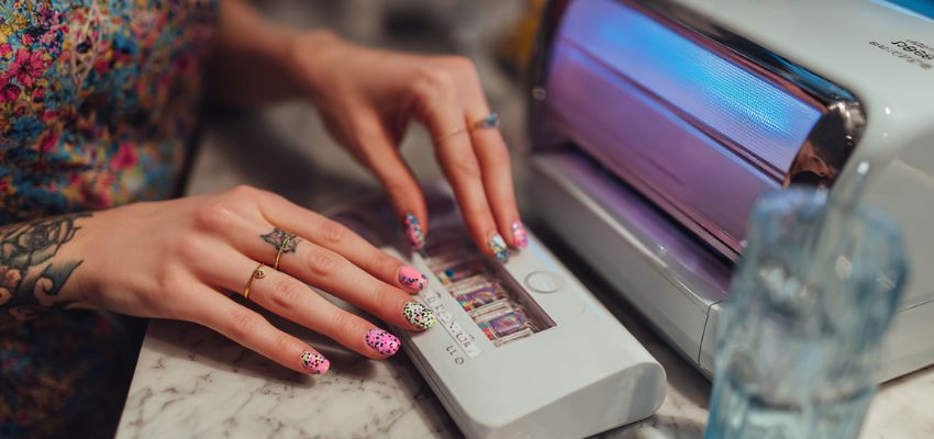 Professional using a high-tech nail printer to apply intricate floral designs with pinpoint accuracy onto artificial nail tips, showcasing advanced nail printing technology.