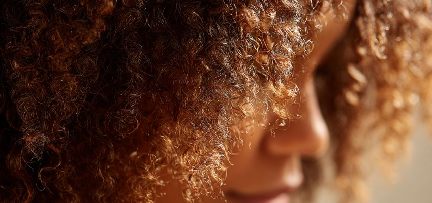 Close-up profile of a person with healthy, defined curly hair, highlighting natural hair cuticle types in textured curls.