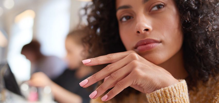 A woman with freshly painted pink nails rests her hand near her face to display the final result of a manicure in how long does a manicure take.